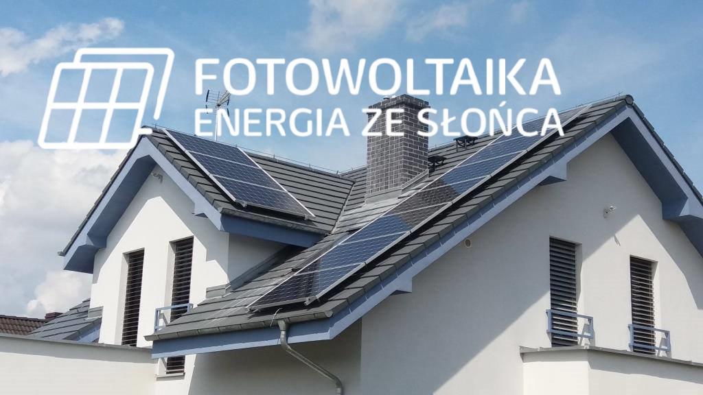 Panele słoneczne na dachu dwuspadowym jasnego domu z szarymi elementami wykończeniowymi i kominem z cegły, częściowo zasłonięte przez biały napis z nazwą usługi.