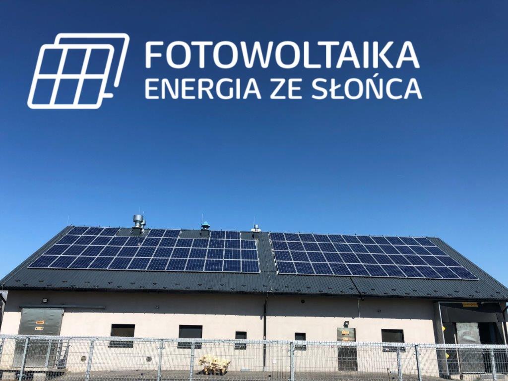 Instalacja paneli słonecznych na dachu budynku przemysłowego pod błękitnym niebem, z widocznym logo firmy z napisem 'Fotowoltaika Energia ze Słońca'.