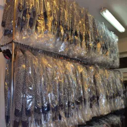 Rzędy ubrań w foliowych pokrowcach na wieszakach w magazynie, widoczne wzory w kropki na odzieży, oświetlenie jarzeniowe.