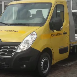 Żółty samochód pomocy drogowej marki Renault Master z napisem 'Pomoc Drogowa' na masce i drzwiach, zaparkowany na zewnątrz budynku z odbijającymi się w szybach samochodami.