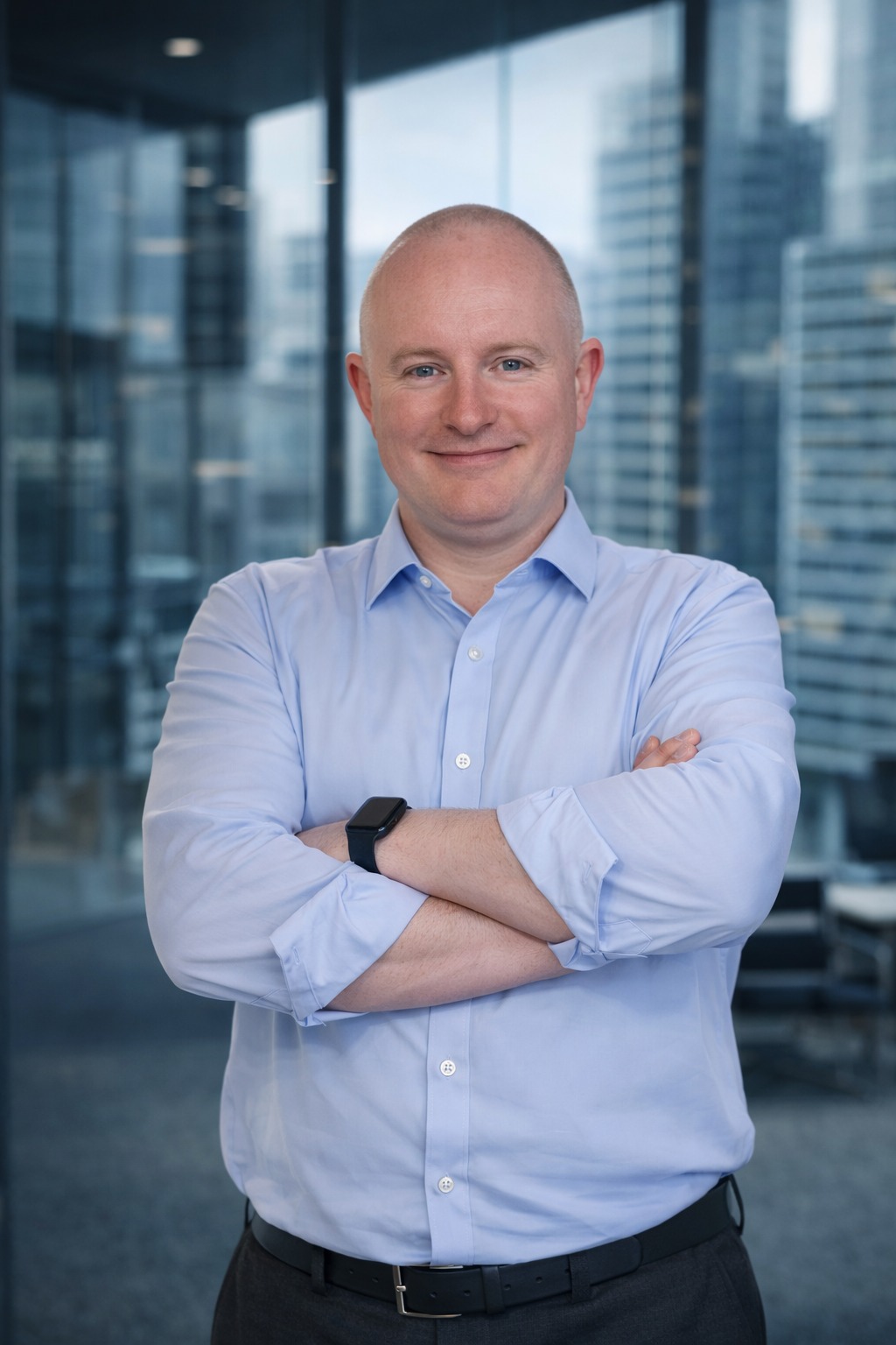 Portret mężczyzny w błękitnej koszuli z założonymi rękami na tle biurowca. Widoczny zegarek na nadgarstku i delikatny uśmiech. Profesjonalny wizerunek.