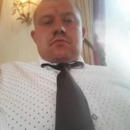 Portret mężczyzny we Wrocławiu w koszuli w kropki i krawacie, z żyrandolem w tle. Ujęcie z dołu.