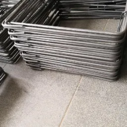 Stosy kwadratowych, giętych prętów zbrojeniowych ułożone na szarej, ceramicznej podłodze, widoczne ślady magazynowania.