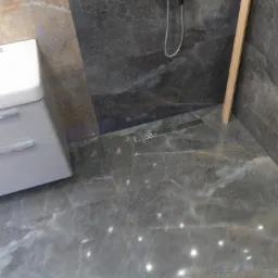 Wykończona łazienka z szarymi marmurowymi płytkami, widoczny odpływ liniowy, bateria prysznicowa i fragment toalety.