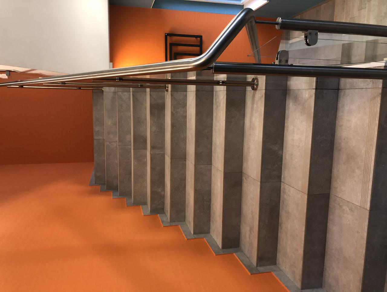Schody z szarymi płytkami i metalową balustradą, pomarańczowa podłoga i ściana. Widok z góry, nowoczesne wykończenie wnętrza, kontrastowe kolory.