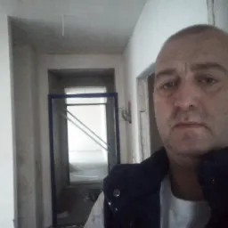 Korytarz w trakcie remontu, widoczna konstrukcja pod zabudowę z płyty karton-gips, surowy stan ścian i sufitu, oraz osoba w ubraniu roboczym.