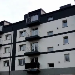 Nowoczesny, czteropiętrowy budynek mieszkalny z balkonami o stalowych balustradach, pomalowany w biało-czarne pasy, widziany pod kątem z dołu.