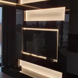 Nowoczesna ściana telewizyjna z czarnego lakierowanego MDF z podświetleniem LED, widok na miasto za oknem.