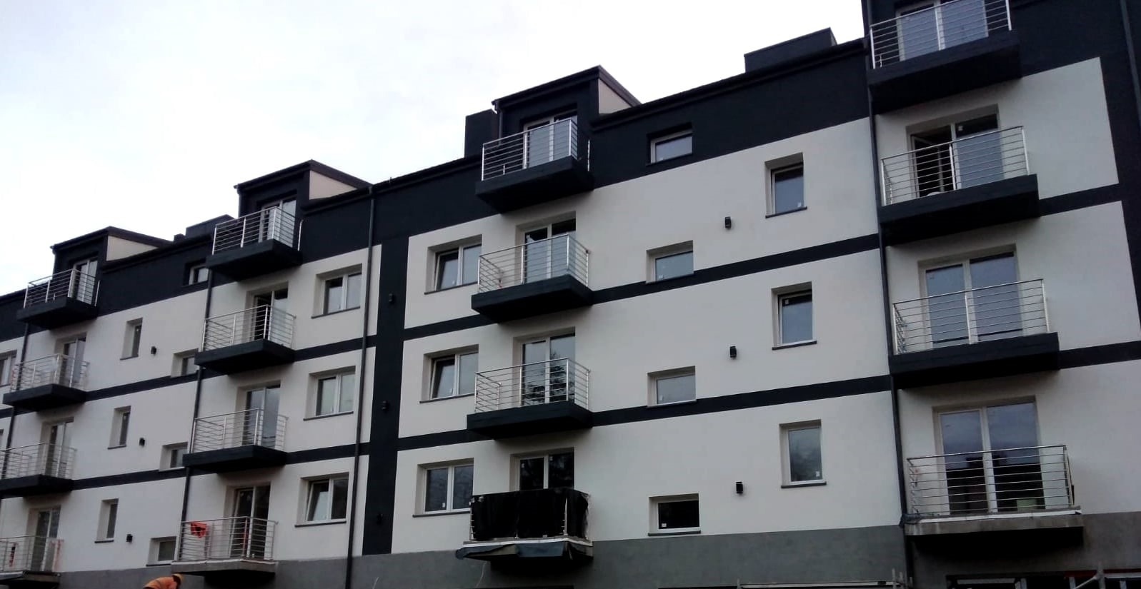 Nowoczesny, czteropiętrowy budynek mieszkalny z balkonami o stalowych balustradach, pomalowany w biało-czarne pasy, widziany pod kątem z dołu.