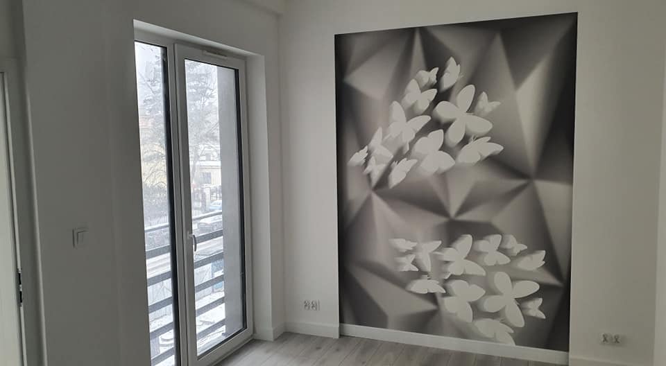 Świeżo wykończone wnętrze pokoju w Łasku z fototapetą 3D z motywem motyli na jednej ze ścian, widoczne również okno balkonowe i panele podłogowe.