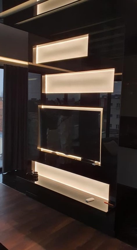 Nowoczesna ściana telewizyjna z czarnego lakierowanego MDF z podświetleniem LED, widok na miasto za oknem.