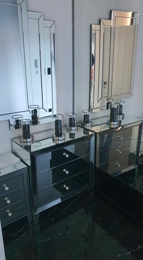 Komplet mebli do sypialni w stylu glamour: dwie czarne komody z lustrzanymi frontami, kryształowe gałki, lustra w artdecowskich ramach i czarna marmurowa podłoga.