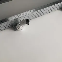 Kamera monitoringu Hikvision zamontowana na metalowej szynie pod sufitem w Krakowie, widok z dołu.