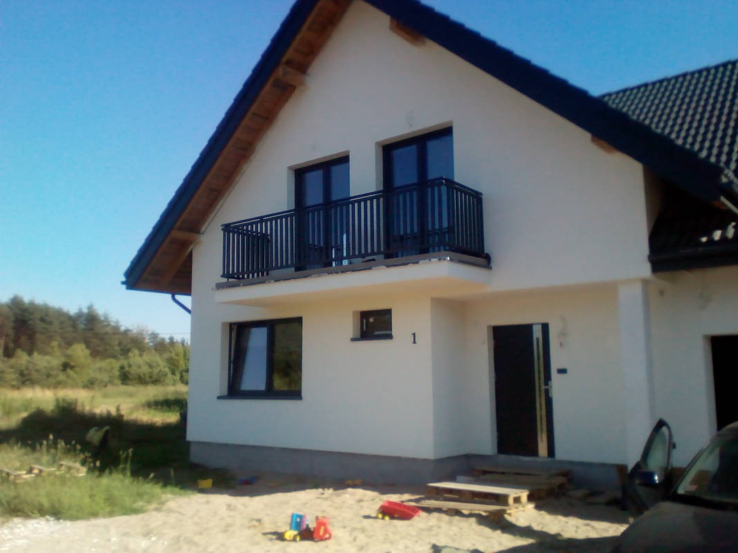 Nowy, biały dom jednorodzinny z czarnymi oknami i balkonem, widoczny z zewnątrz, z piaskiem i zabawkami na pierwszym planie.