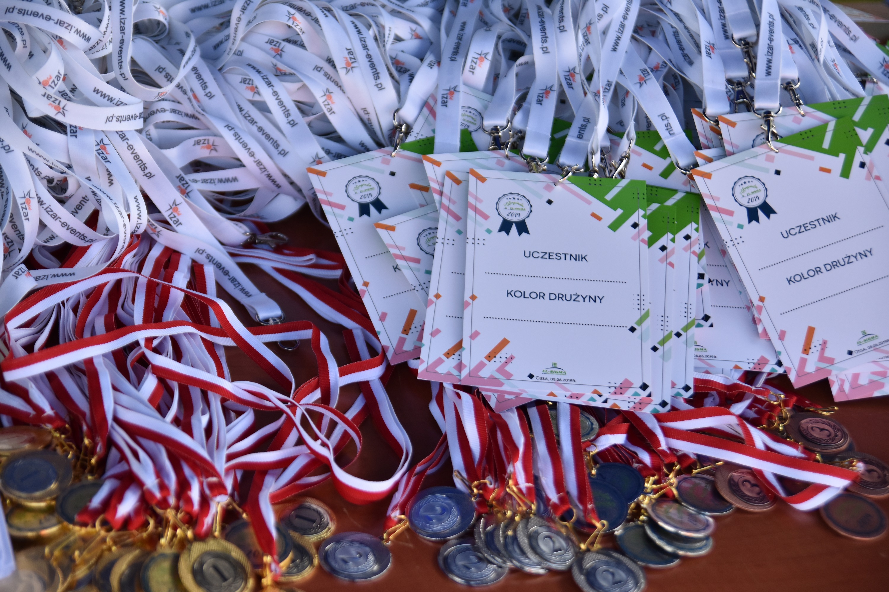 Identyfikatory uczestników z logo firmy, białe smycze z nadrukiem i medale za miejsca na brązowym tle.