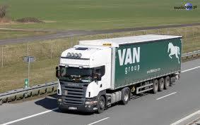 Ciągnik siodłowy Scania z naczepą VAN Group, widziany z boku na autostradzie, z widocznym znakiem drogowym w tle.