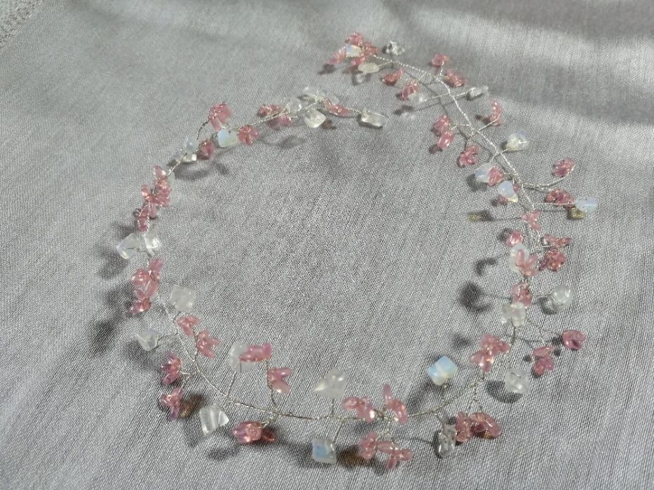 Delikatna ozdoba do włosów z różowych i białych koralików na srebrnym drucie, leżąca na szarym, lekko błyszczącym materiale.