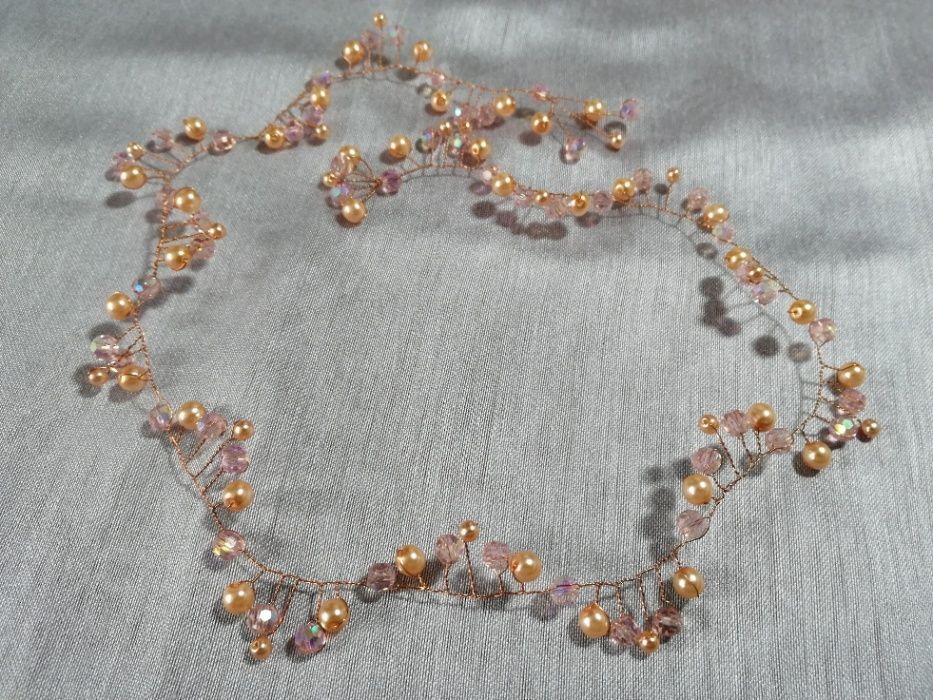 Delikatna ozdoba do włosów z miedzianego drutu, perełek w odcieniach brzoskwini i kryształków, ułożona na srebrzystym tle.