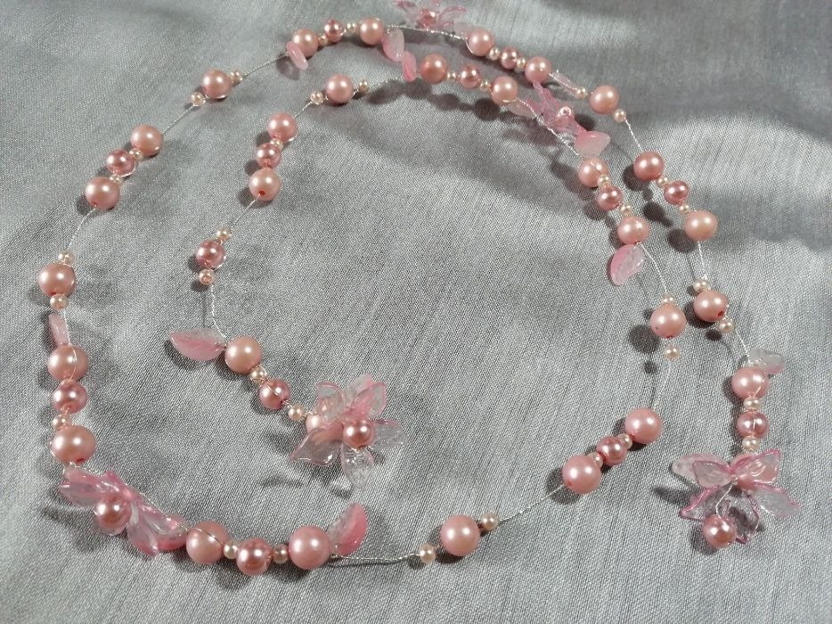 Delikatny naszyjnik z różowych perełek i przezroczystych kwiatków na srebrnym druciku, ułożony na szarym tle.