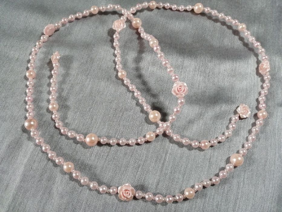 Delikatny, ręcznie robiony naszyjnik z różowych perełek i ozdobnych różyczek, leżący na srebrzystej tkaninie.