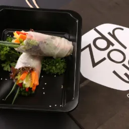 Dwa wiosenne sajgonki z warzywami w czarnym pudełku na wynos, z logiem firmy cateringowej z Miłek w tle.