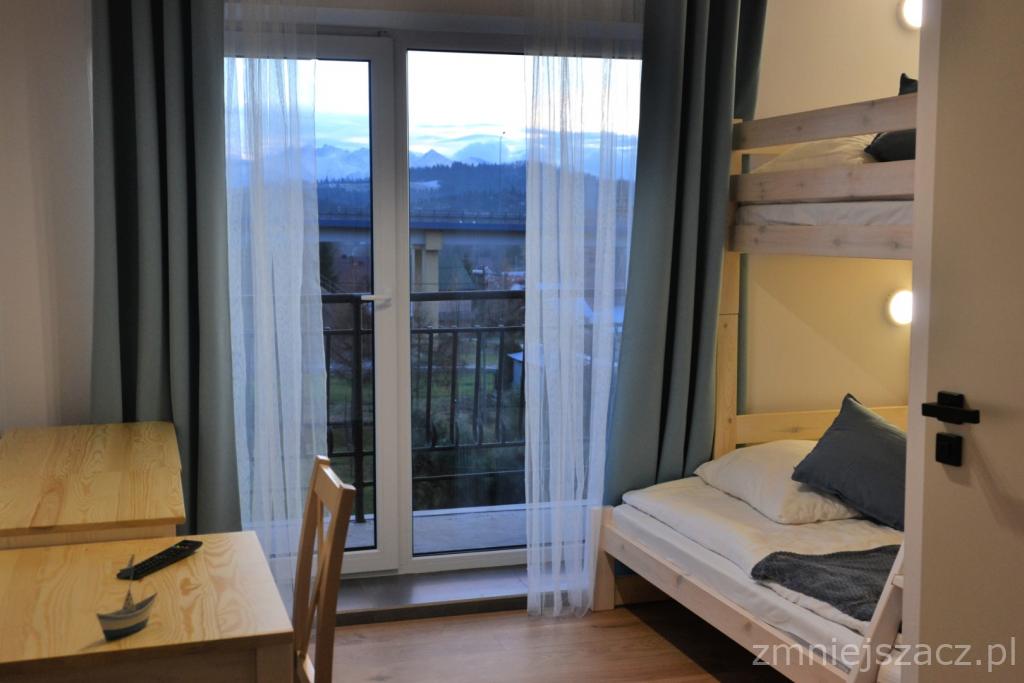 Pokój z łóżkiem piętrowym i biurkiem, widok na góry przez balkon.