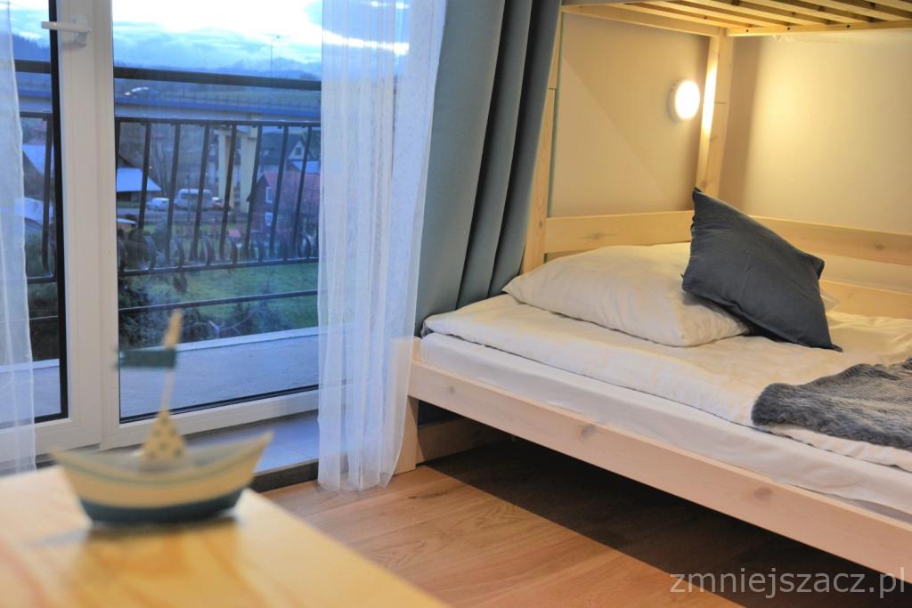 Pokój z łóżkiem piętrowym, widokiem na góry przez balkon i dekoracyjną łódką na stoliku.
