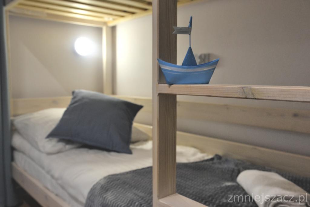 Drewniane łóżko piętrowe z szarą pościelą i dekoracyjną, niebieską łódką na półce w pokoju w Kluszkowcach.