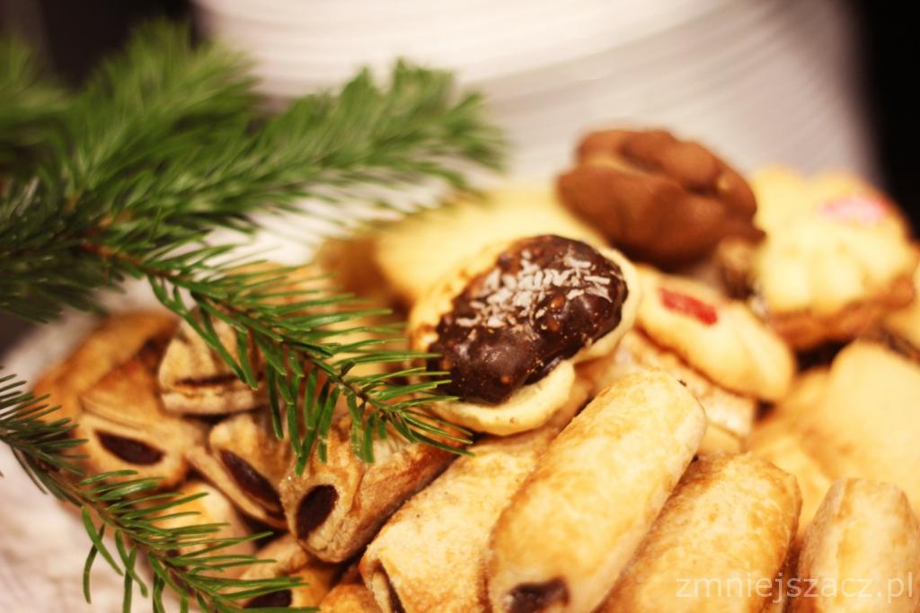 Świąteczne ciasteczka na paterze udekorowane gałązką świerku, z bliska widoczne roladki z nadzieniem, ciastka z czekoladą i posypką kokosową oraz inne kruche ciasteczka.