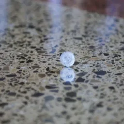 Polerowana posadzka przemysłowa z widocznym wzorem kamieni i żywic, odbijająca światło i monetę 1 zł, leżącą na powierzchni dla skali.