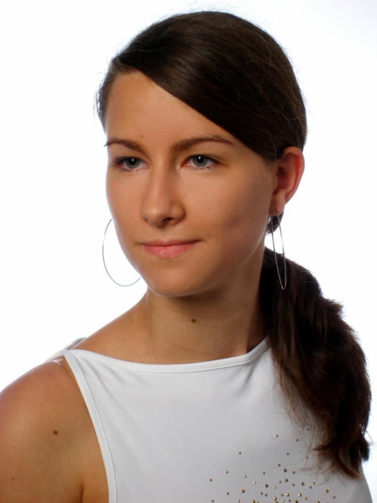 Portret młodej kobiety z ciemnymi włosami spiętymi w kucyk, ubrana w białą bluzkę z delikatnymi zdobieniami, z kolczykami kołami na białym tle.