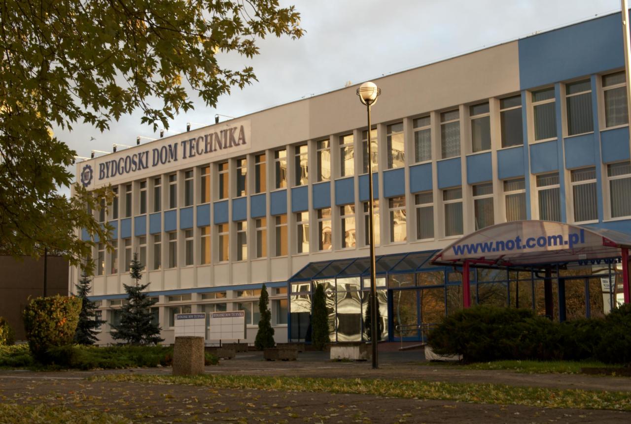 Budynek Bydgoskiego Domu Technika z niebieskimi akcentami, widok z zewnątrz w jesiennej scenerii, oświetlony popołudniowym słońcem odbijającym się w oknach.