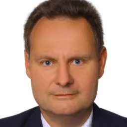 Portret biznesowy mężczyzny w ciemnym garniturze, z jasnymi oczami, na białym tle. Ujęcie od przodu, twarz wyraźna, oświetlenie równomierne.
