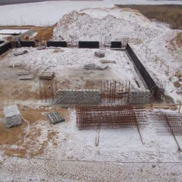 Fundamenty domu w trakcie budowy w Warszawie, częściowo przykryte śniegiem, widoczne zbrojenia i bloczki betonowe.