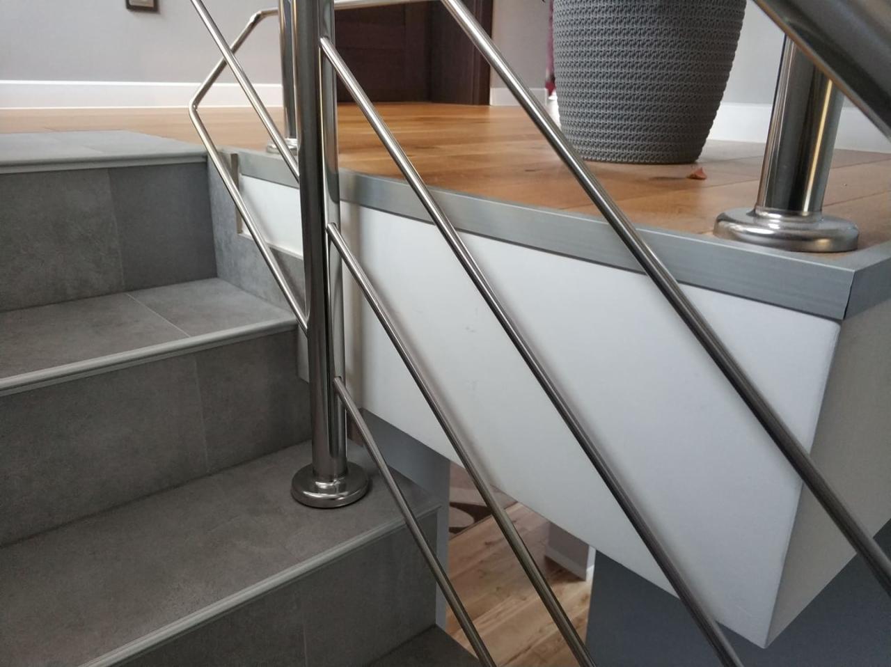 Wykończone schody z szarymi płytkami i metalową balustradą, widok z dołu, na górze drewniana podłoga i donica.