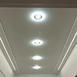 Biały, podwieszany sufit z wbudowanymi okrągłymi lampami punktowymi i liniowym oświetleniem LED po bokach w nowocześnie wykończonym wnętrzu.