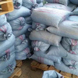 Stos worków z zawartością ułożonych na paletach, widoczne czerwone pasy na workach i szare tło