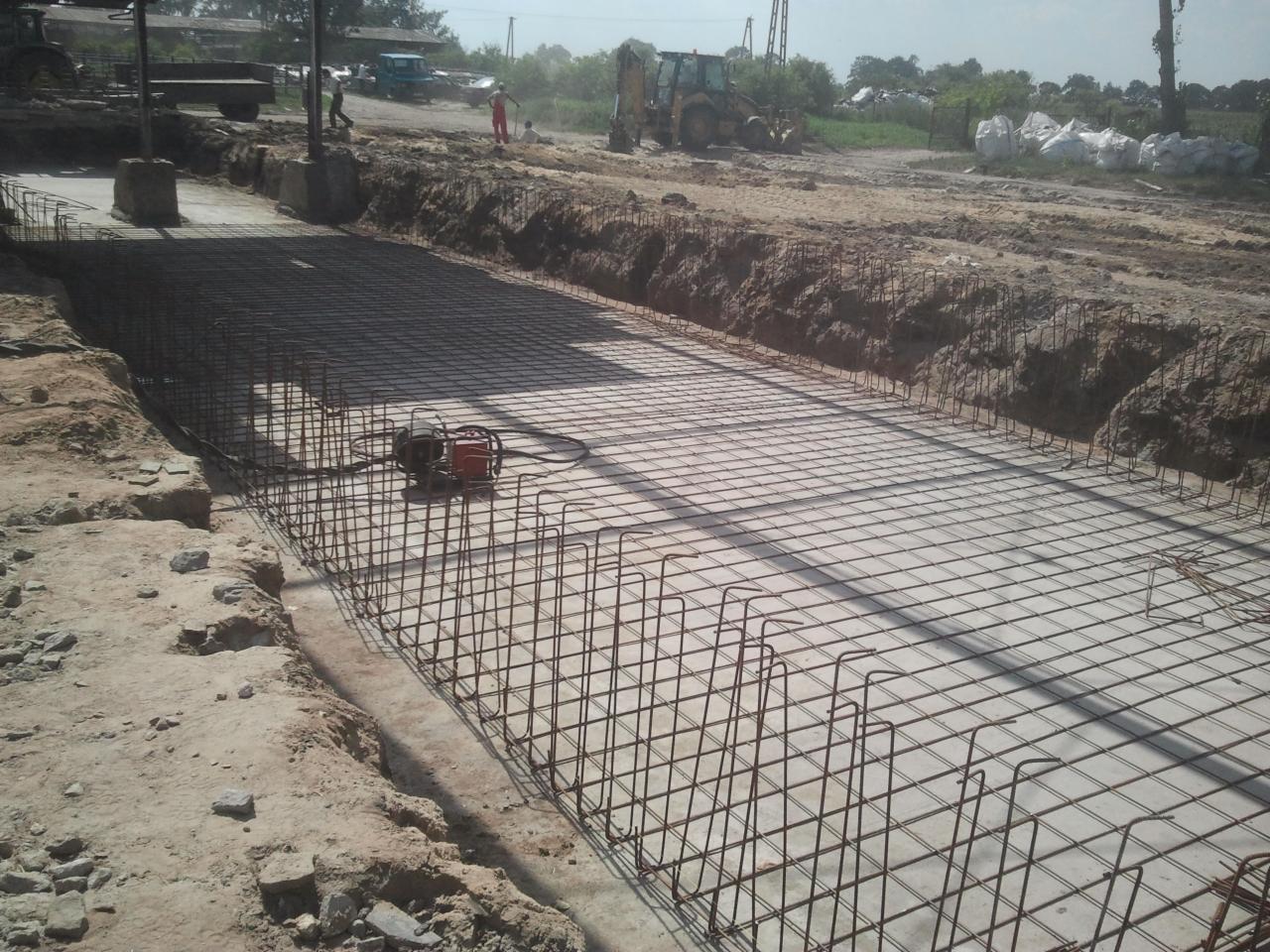 Zbrojenie fundamentu pod budowę drogi, widoczne siatki stalowe i sprzęt budowlany na placu. Ujęcie z perspektywy gruntu, podkreślające rozległość prac.