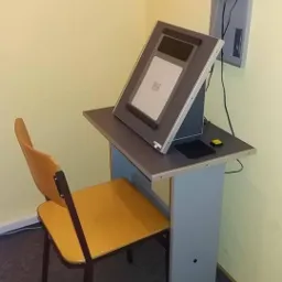 Aparat do badania wzroku z tablicą optotypów i żółtym krzesłem w gabinecie.