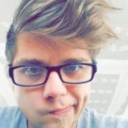 Młody mężczyzna w okularach robi selfie na tle ściany z płyt kartonowo-gipsowych przed szpachlowaniem.