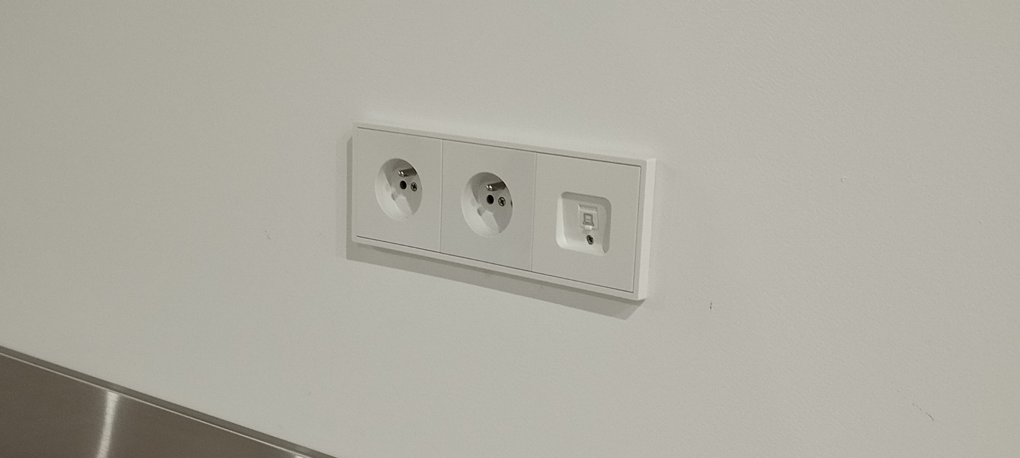 Biały panel ścienny z dwoma gniazdkami elektrycznymi i gniazdem niskoprądowym w nowym budynku.