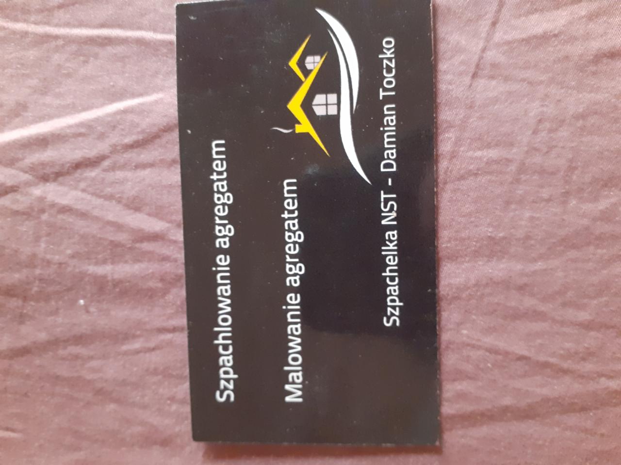 Wizytówka firmy Szpachelka NST - Damian Toczko, oferującej usługi szpachlowania i malowania agregatem, z logo przedstawiającym zarys domu.