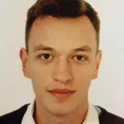 Portret młodego mężczyzny w ciemnej marynarce i jasnej koszuli na jasnym tle. Zdjęcie paszportowe z delikatnym uśmiechem.