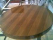 Błyszczący, okrągły blat drewniany po lakierowaniu, widoczny układ słojów pod kątem, na metalowym stelażu.