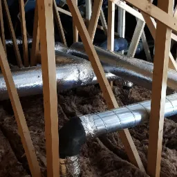 Instalacja przewodów wentylacyjnych w przestrzeni poddasza, widoczne drewniane elementy konstrukcyjne oraz izolacja z wełny mineralnej.