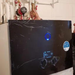 Instalacja pompy ciepła Daikin: widoczne rury, zawory, pompa obiegowa Grundfos oraz niebieski zbiornik wyrównawczy. Na froncie pompy folia ochronna i podświetlony ekran z parametrami pracy.