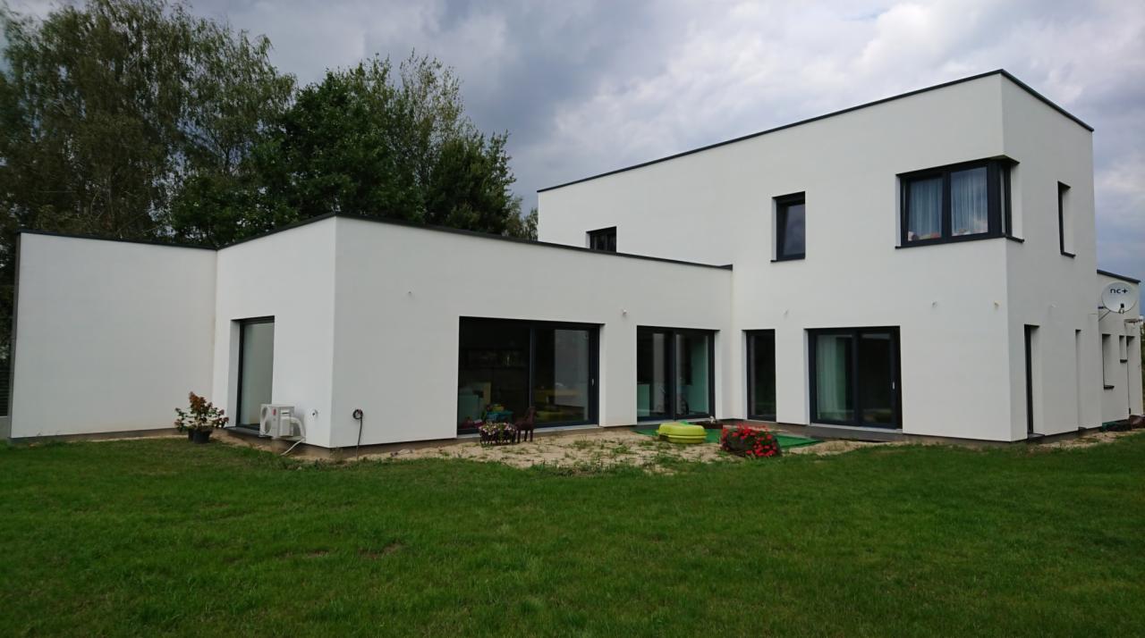 Nowoczesny, biały dom jednorodzinny z czarnymi ramami okien i przesuwnymi drzwiami tarasowymi, widok z ogrodu na elewację z zamontowaną anteną satelitarną.