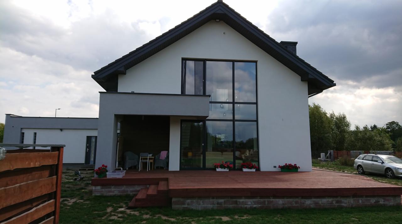 Nowoczesny dom jednorodzinny z dużymi, czarnymi oknami i tarasem z desek kompozytowych, widok z zewnątrz w pochmurny dzień.