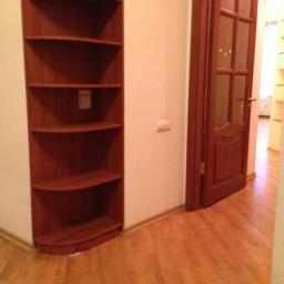 Janos - Wnętrze pokoju z narożną, drewnianą półką, brązowymi drzwiami z szybkami i laminowaną podłogą w odcieniach brązu.