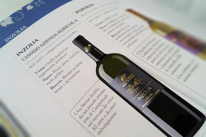 Butelka białego wina Inzolia leżąca na otwartej książce z opisem wina, etykieta z nazwą producenta Candido Azienda Agricola i regionem Sicilia.